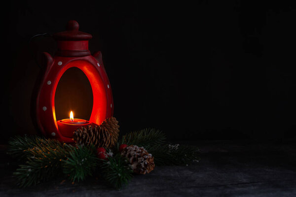 Горящие свечи и рождественские украшения на тёмном фоне. Концепция Нового года. Схема праздничной открытки. Восковая свеча в красном глиняном подсвечнике. Уютная рождественская атмосфера. Копирование пространства