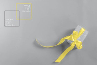 Gri arka planda sarı fiyonklu bir kutuda hediye. 2021 yılının renkleri Ultimate Gray ve Aydınlatıcı renklerdir. Düz bir düzlemin üst görüntüsü. Mutlu Noeller, yeni yıl, tatil kartı tasarımı