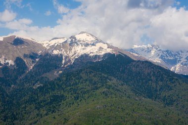 Karla kaplı dağlar ve yeşil orman. Kafkaslar 'ın sıradağları. Dağlarda ilkbahar güneşli bir gün. Baharda renkli bir manzara. Eko-turizm, seyahat, kışın açık hava aktiviteleri.