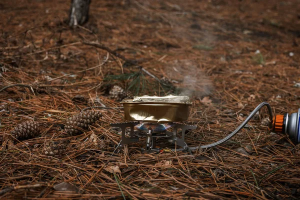 Tourist gas burner for heating food. Open fire close-up. Metal portable small burner in the forest on coniferous litter. The concept of hiking, tourism, outdoor activities. Warming up tourist food