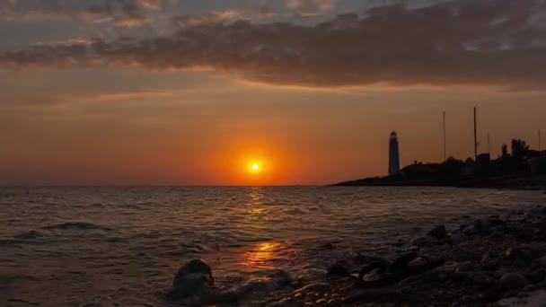 灯台の眺めとタイムラプスの夕日 黄金の暖かい色合いでカラフルな大気の風景 オレンジの空 丸い太陽がゆっくりと地平線の下に沈みます 波はすぐに岸に上がり — ストック動画