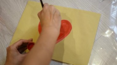 Bir kız kağıda kırmızı akrilik boyalı bir kalp çizer. Aşkın sembolü, Sevgililer Günü, duygular. Yaratıcı ambalaj - Sevgililer Günü kartı. Bayram havası konsepti. 14 Şubat için hediye.