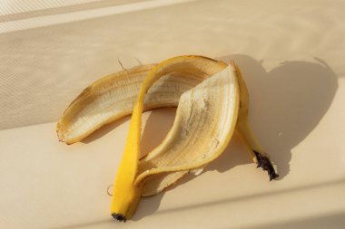 Açık bej arkaplan manzaralı muz kabuğu. Organik çöp. Ayrı yiyecek atığı koleksiyonu kavramı. Doğal güneş ışığı ve zıt gölgeler. Çevreyi koruma.