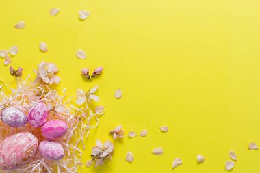 Renkli yumurtaların ve badem çiçeklerinin sarı katı arkaplandaki paskalya kompozisyonu. Mutlu Paskalyalar. Pastel renklerde yumuşak düz bir düzen. Üst görünüm, boşluğu kopyala. Yaratıcı estetik tebrik kartı.