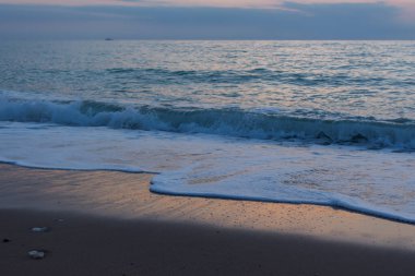 Deniz kumu akşamı. Deniz kıyısında gün batımından sonraki mavi saat. Güneşin son ışınları dalgalara yansıyor. Parlayan deniz köpüğü sahile yuvarlanıyor. Yaz tatili konsepti, rahatlama, mahremiyet