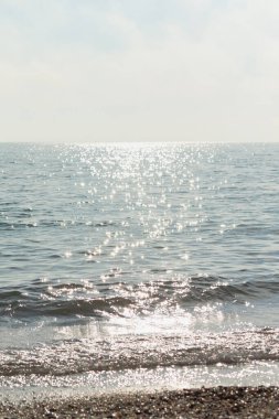 Gümüş deniz ışıl ışıl arka plan. Grinin ve gümüşün gölgeleriyle minimalist yaz manzarası. Gün ortası sıcak. Parlak güneş dalgalara yansıyor. Kopya alanı ile doğal dikey arkaplan