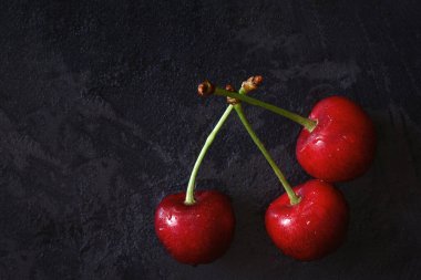 Kiraz ağacı makro siyah arkaplan üstü görünümü. Masanın üzerinde sulu kiraz meyveleri ve su damlaları var. Tazelik, düzgün beslenme, vitaminler. Gösterişsiz fotoğraf. Boşluğu kopyala