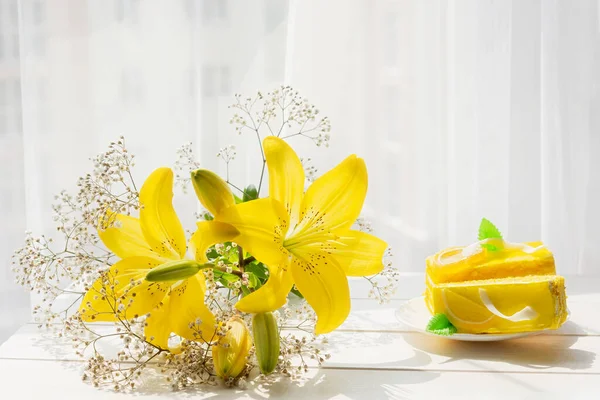 Yellow cake yellow lilies on a white wooden background in bright sunlight. Flowers cake for the holiday. The concept of a birthday, congratulations, romantic mood. Trending illuminated yellow color