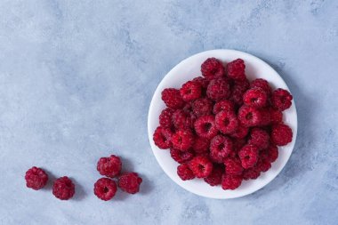 Ahududu tabağı gri masa manzaralı beyaz. Yakından bakınca olgun ahududu. Yaz yemeği, tazelik, vitaminler. Gri arka planda güzel meyveler. Yaz diyeti sağlıklı tatlı