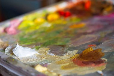 Beyaz yağlı boya kaplamalı sanatçı paleti. Bulanık renkli arka plan. Ressamın seçici odaklı profesyonel resimleri. Yaratıcılık kavramı, yaratıcı fikirler, favori bir hobi..