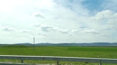 Yeşil tarlalar yol arabası penceresi. Yeşil bahar buğday tarlalarının yan penceresinden ve mavi gökyüzünde süzülen bulutlardan bak. Rusya 'nın yollarında seyahat, araba penceresinden nefes kesici bir manzara.