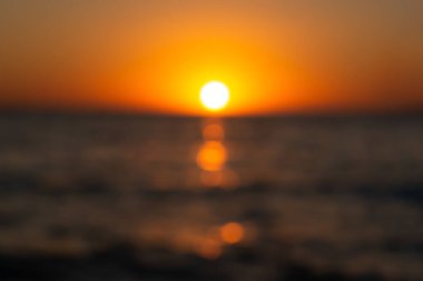 Yaz güneşi bulanık bir günbatımı arka planıdır. Yaz tasarımı için ateşli bir arka plan. Güzel Bokeh, parlak deniz, gün batımının ılık ışınları ya da şafak. Yuvarlak sarı güneşin soyut arkaplan görüntüsü