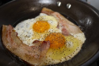 İki yumurta ve domuz pastırmalı siyah tava.