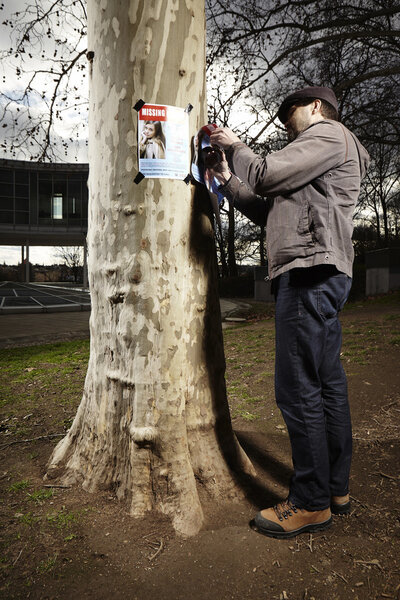 Полицейский в парке вешает плакат о пропаже человека
