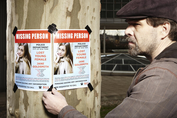 Полицейский заклеивает плакат о пропаже человека на дерево в парке
