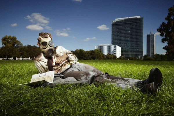 Gestionnaire sale en masque à gaz avec ordinateur portable posé sur l'herbe — Photo