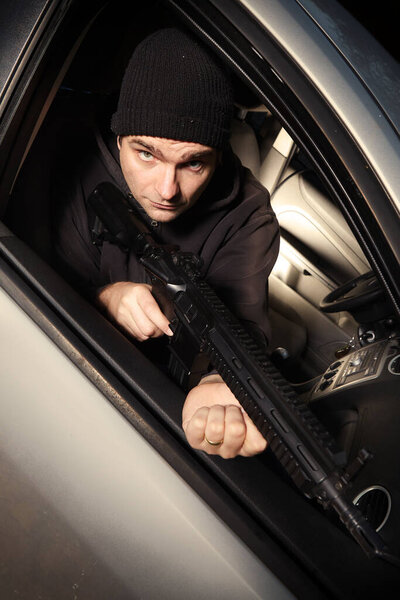 Man with assault carbine waiting for his wictim inside car