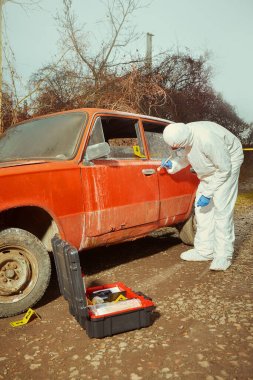 Older red car burned by criminals examined by police technician clipart