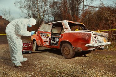 Older red car burned by criminals examined by police technician clipart