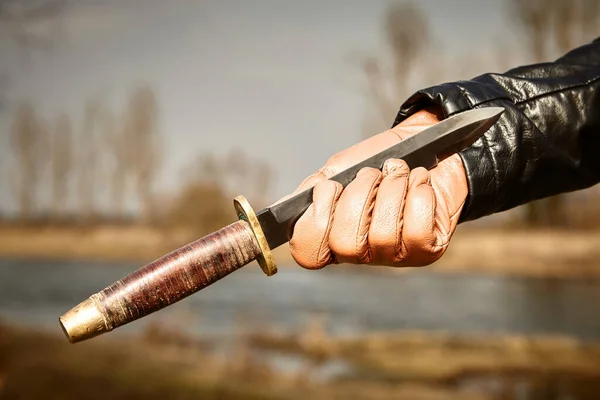 Detail of throwing knife holding in hand dressed in leather glove