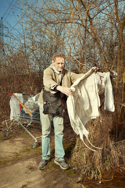 Пожилой бездомный стирает свою одежду в наружной воде
