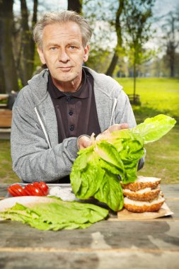 Şehir parkındaki adam hamburger yemeği için malzeme hazırlıyor.