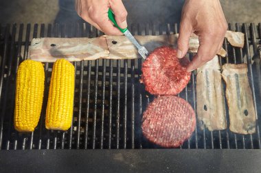 Şehir parkındaki adam yemeği için biftek köftesi pişiriyor.