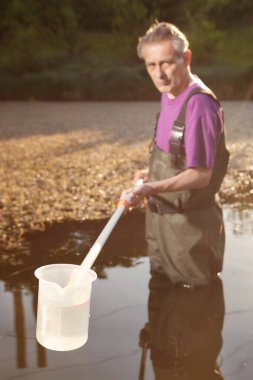 Water quality analyst dressed in chest wader collecting samples