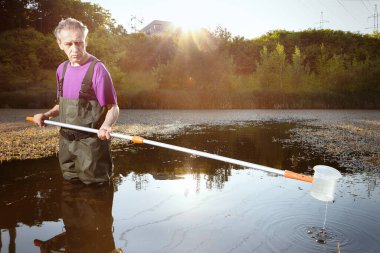 Water quality analyst dressed in chest wader collecting samples