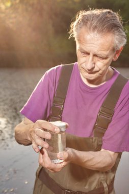 Water quality analyst dressed in chest wader closing bottle with water sample