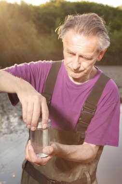 Water quality analyst dressed in chest wader closing bottle with water sample