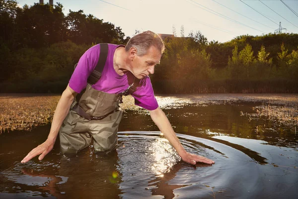 Water quality analyst dressed in chest wader collecting samples