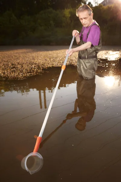 Water quality analyst dressed in chest wader collecting samples