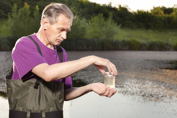 Water quality analyst dressed in chest wader closing bottle with water sample