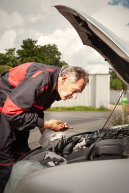 Adam genel olarak arabasının açık motoru üzerinde çalışıyor.