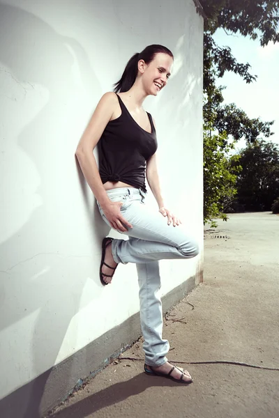 Sonriente chica morena por la pared — Foto de Stock