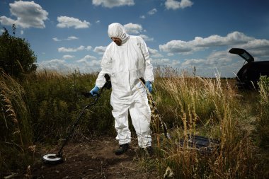 Criminologist technician exploring place with metal detector