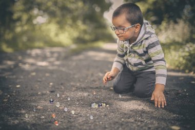 Tozlu yolda küçük bir çocuk doğada klasik misketleri eğitiyor.