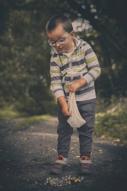Tozlu yolda küçük bir çocuk doğada klasik misketleri eğitiyor.