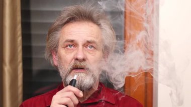 Yaşlı adam detaylı video görüntülerinde kapalı mekanda elektronik sigara içiyor.