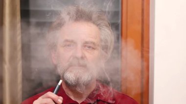 Yaşlı adam detaylı video görüntülerinde kapalı mekanda elektronik sigara içiyor.