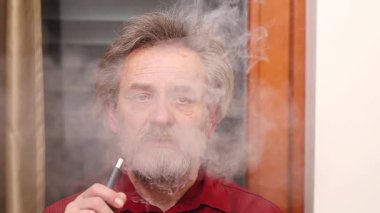 Yaşlı adam detaylı video görüntülerinde kapalı mekanda elektronik sigara içiyor.