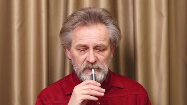 Yaşlı adam detaylı video görüntülerinde kapalı mekanda elektronik sigara içiyor.