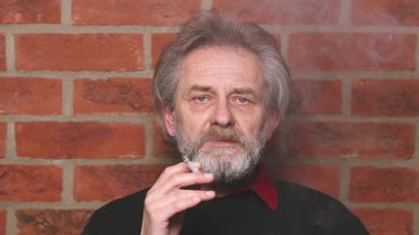 Yaşlı adam balkonda sigara içiyor. Detaylı video çekimlerinde klasik sigara.