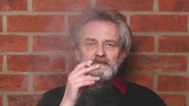 Yaşlı adam balkonda sigara içiyor. Detaylı video çekimlerinde klasik sigara.