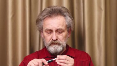 Yaşlı adam detaylı video görüntülerinde kapalı mekanda elektronik sigara içiyor.