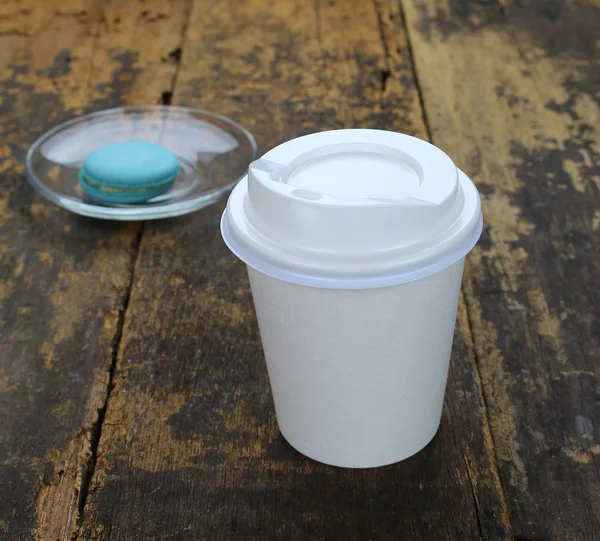 White paper cup of coffee and macaroon on a wooden table