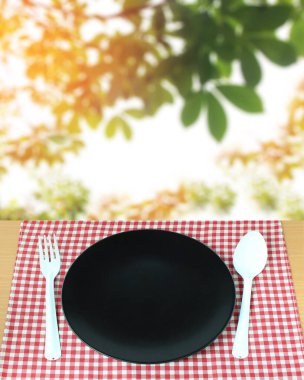 çatallı kaşık ve kareli masa örtüsü ve bulanık yapraklı arka plan