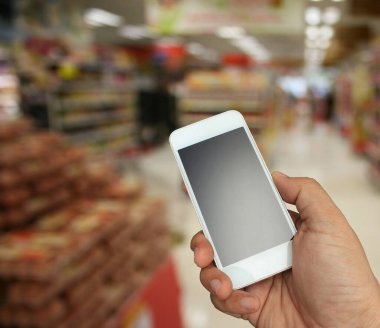Arka plan bulanık bir şekilde akıllı telefonu süpermarkette tutuyor.