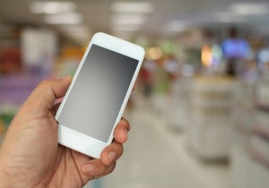 Arka plan bulanık bir şekilde akıllı telefonu süpermarkette tutuyor.